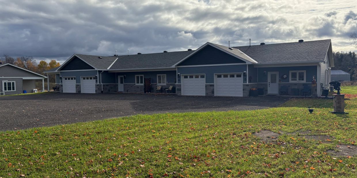 A large blue duplex with white garage doors under a cloudy sky.