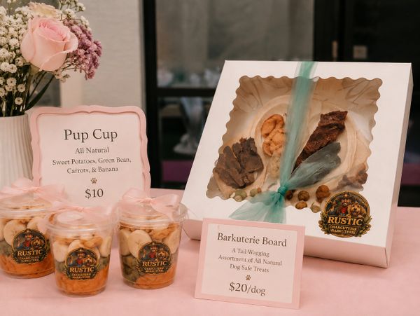 Rustic dog treats display with Pup Cups and Barkuterie Board on a pink table.