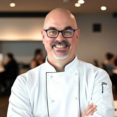 Smiling chef in white uniform and glasses in a restaurant setting.