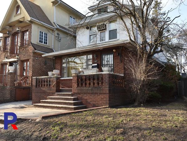 A brick house with a raised porch and leafless trees in front.
