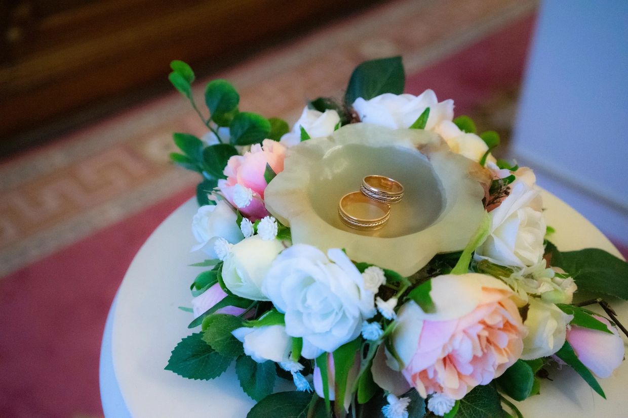 Two wedding rings are in a dish on a table surrounded by wedding flowers. A ring blessing. 