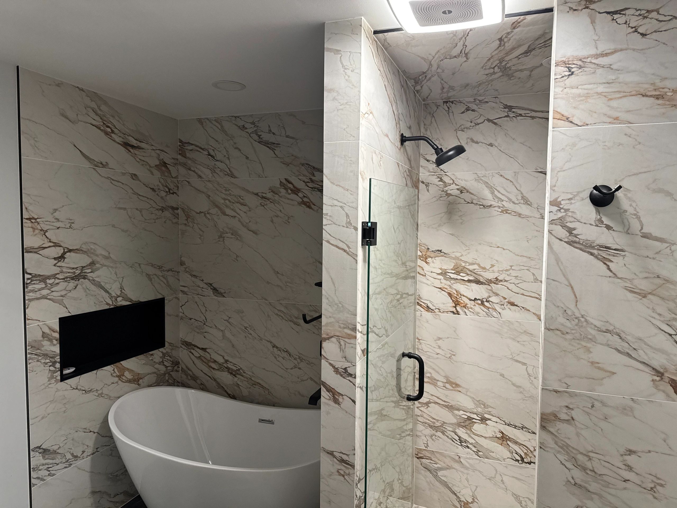 Modern bathroom with marble walls, freestanding bathtub, and glass shower enclosure.