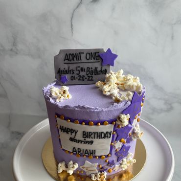 Movie night theme kid's birthday cake in buttercream with a sugar cookie movie ticket and popcorn. 