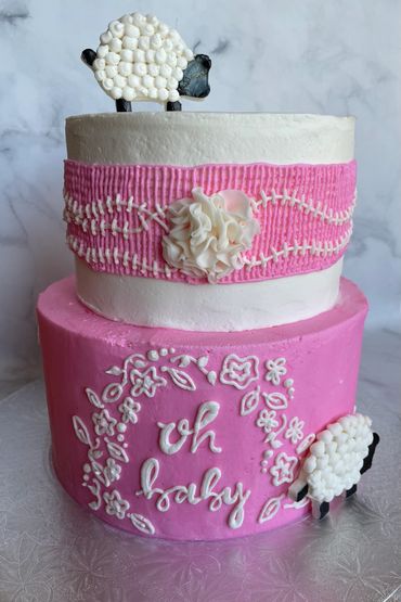 A two tier pink and white buttercream cake with a sheep theme and crosshatch in buttercream. 