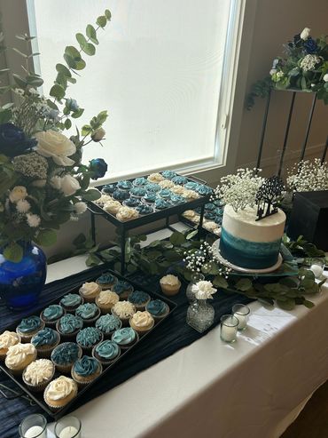A blue and white ombre cake with baby's breath, surrounded by blue and white cupcakes. 