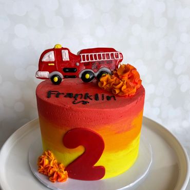 Red, orange and yellow kid's cake with a sugar cookie firetruck on top. 
