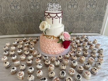 3 tier wedding cake with pink rosettes, artistic gold accents and acrylic topper with mini cupcakes