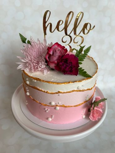Buttercream cake in layers of pink with fresh florals and an acrylic cake topper. 