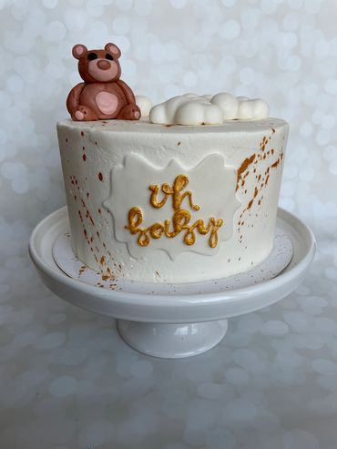 A white buttercream cake with gold splatters and a fondant teddy bear. 