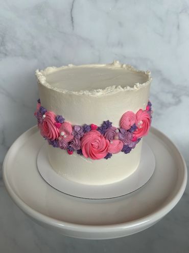 White buttercream cake with rough edge and rosettes around the middle. 