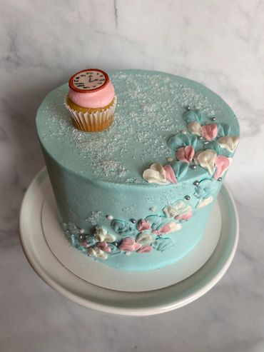 Alice in Wonderland theme cake with buttercream flowers up front and mini cupcake on top. 