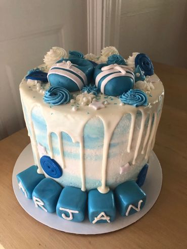 A blue and white ombre buttercream cake with a white drip, and baby shoes and blocks from fondant. 