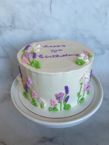 White buttercream cake with buttercream flowers around the sides and top. 