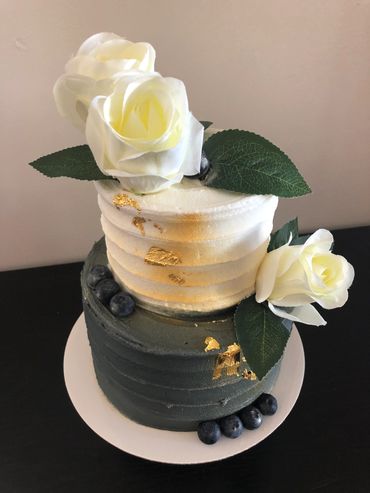 2 tier blue and white buttercream cake with white flowers, gold accent and blueberries. 