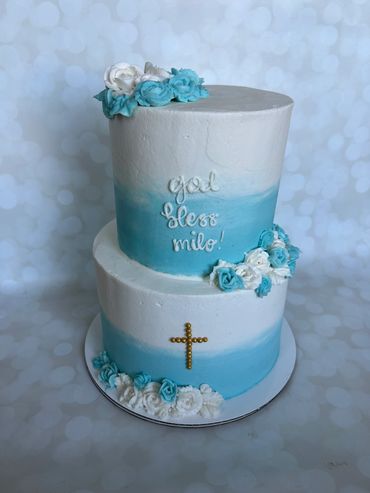 A two tier white and blue ombre buttercream baptism cake with a sprinkle cross and buttercream roses