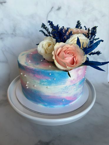 A pink and blue ombre buttercream cake with pink and blue flowers for a gender reveal. 