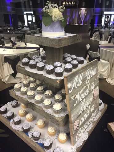White and purple cutting cake with fresh flowers on top of a tower of purple and white cupcakes. 