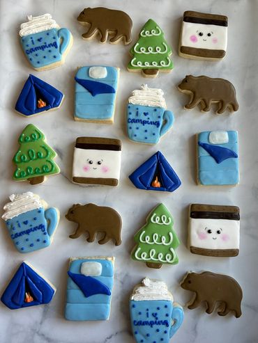 Decorative camping-themed cookies with bears, tents, trees, mugs, and smores. 