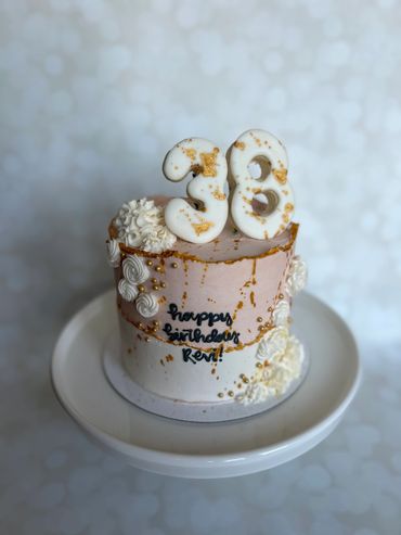 Gold splattered cream and white birthday cake with sugar cookie numbers on top. 