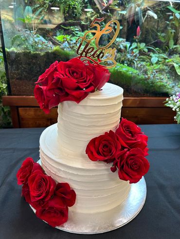 A classic 2 tier buttercream cake in white with red roses. 