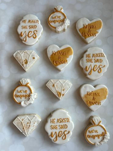 Gold and white theme engagement cookies with a diamond ring and hearts. 