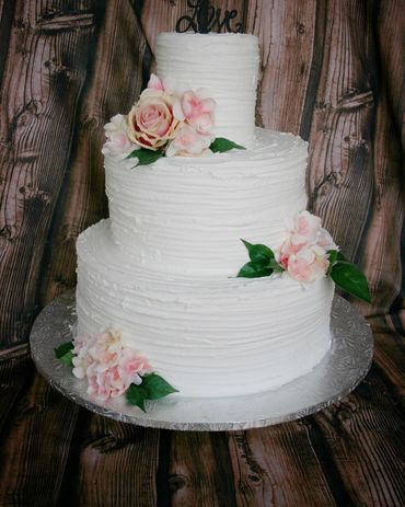 3 tier white buttercream cake with pink silk florals and wood topper. 