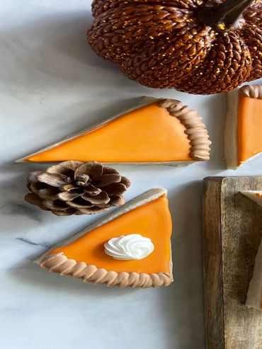 Pumpkin pie slice cookies with a pine cone and decorative pumpkin.