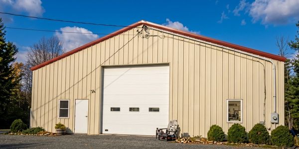 A beige metal garage with a large white door and clear sky.