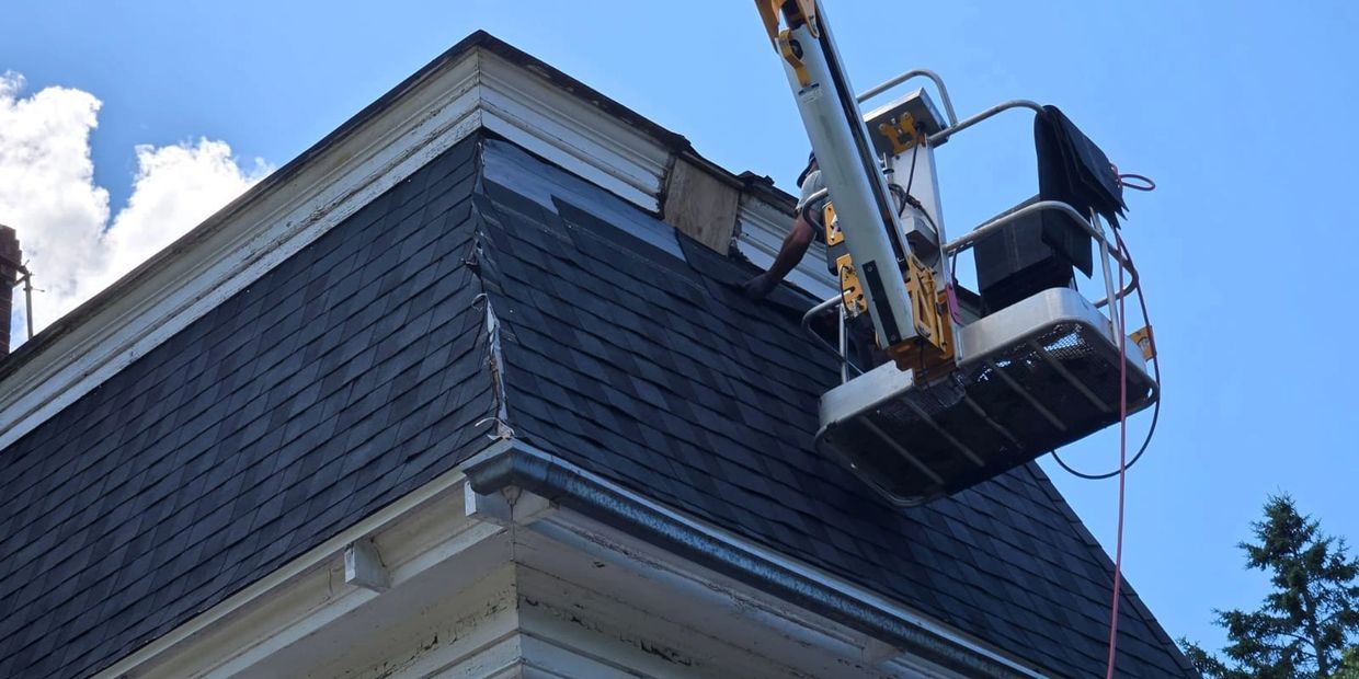 Worker repairing roof shingles from an elevated platform on a sunny day.