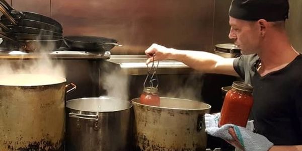 Chef jar-packing sauce from large pots in a kitchen.