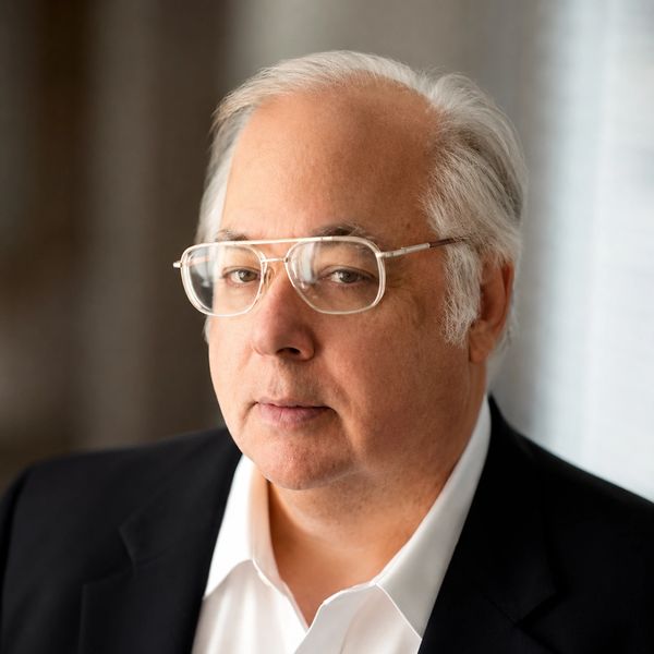 Mature man with white hair and glasses in a suit jacket.