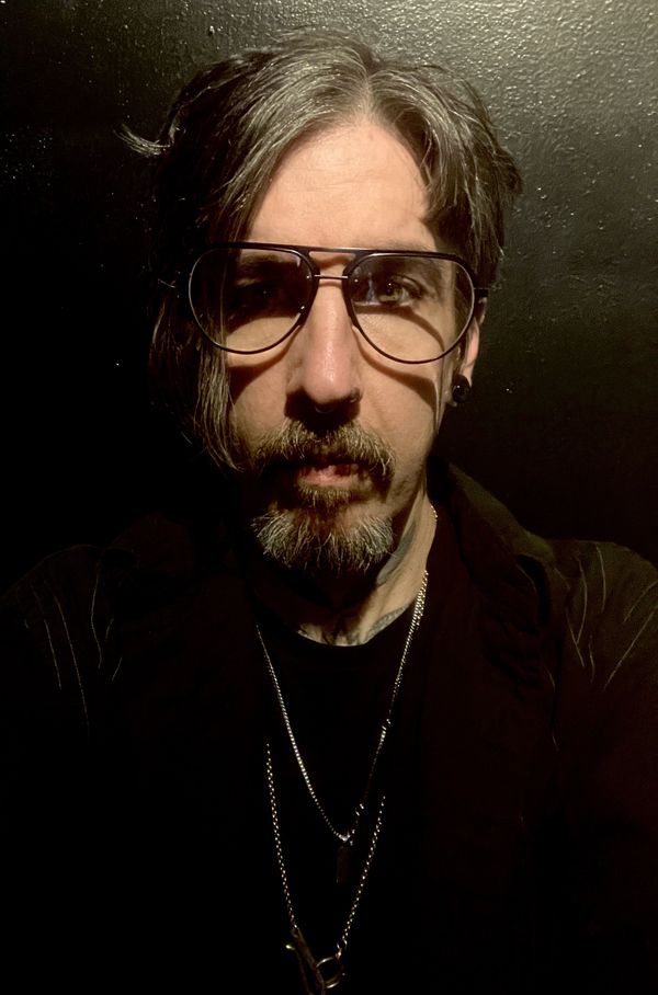 Man with glasses and beard illuminated against a dark background.