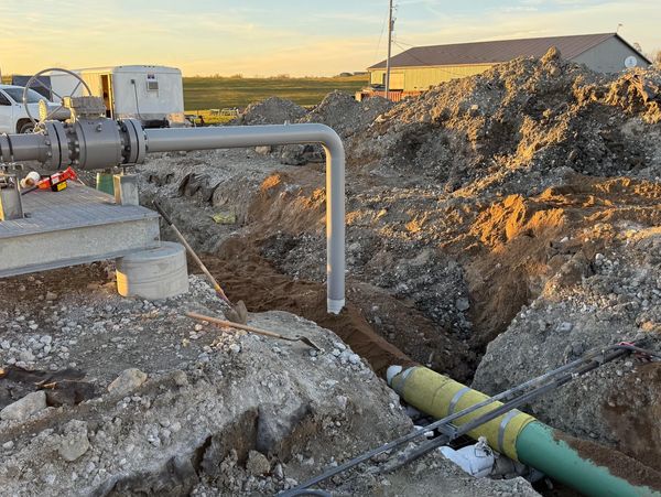 Construction site with large pipes and earthmoving equipment at sunset.