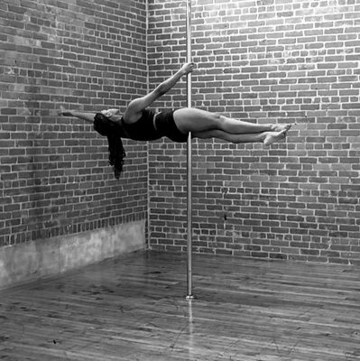 A woman performing a horizontal pole dance move in a studio with brick walls.