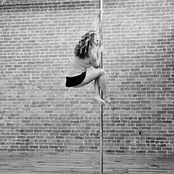 Woman performing a pole dance move against a brick wall.