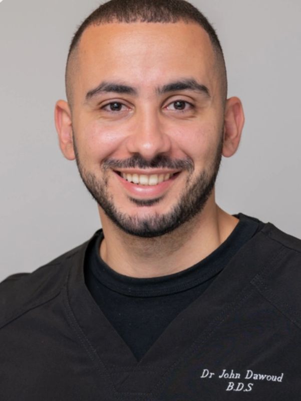Smiling man in black scrubs with name tag Dr John Dawoud, B.D.S.