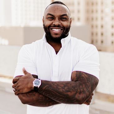 Confident man with tattoos smiling, wearing a white shirt and watch.