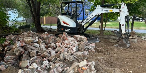 Bobcat excavator next to a pile of broken bricks and rubble outdoors.