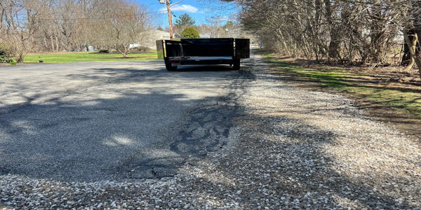 A trailer parked on a partially paved and gravel road on a sunny day.