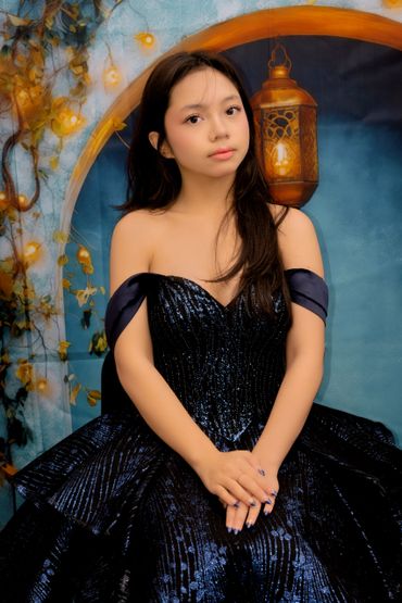 Young woman in an elegant black dress poses with a soft expression.