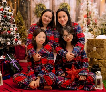 Four women in matching red plaid pajamas posing in a festive Christmas setting.