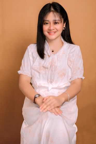 Young woman in white dress smiling against a brown backdrop.