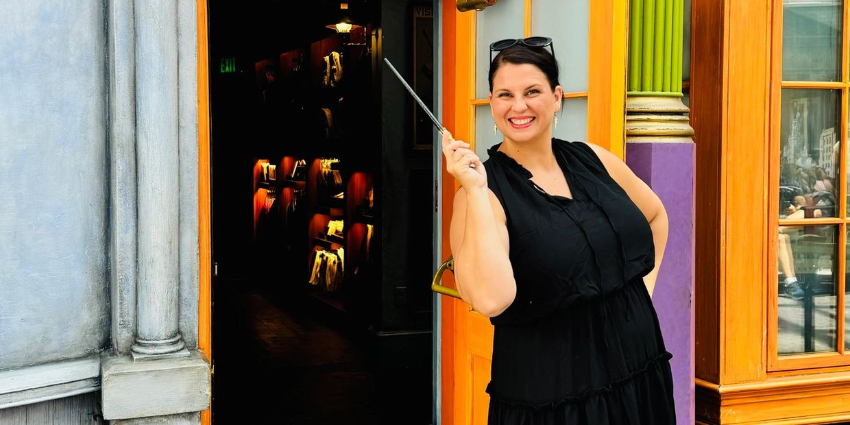 Woman in black dress smiling and holding a wand outside a colorful doorway.