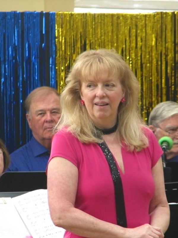 Woman in pink shirt standing in front of a musical group with colorful backdrop.