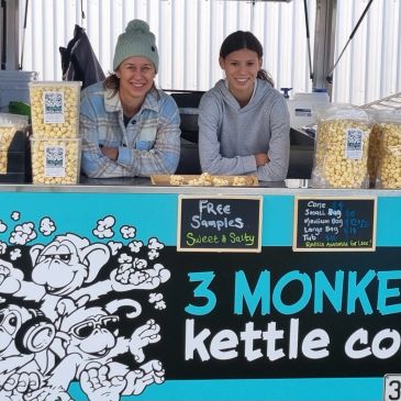Two women selling popcorn at a kettle corn stand.