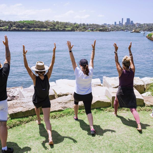 Group practicing yoga near a waterfront with city skyline in the background.