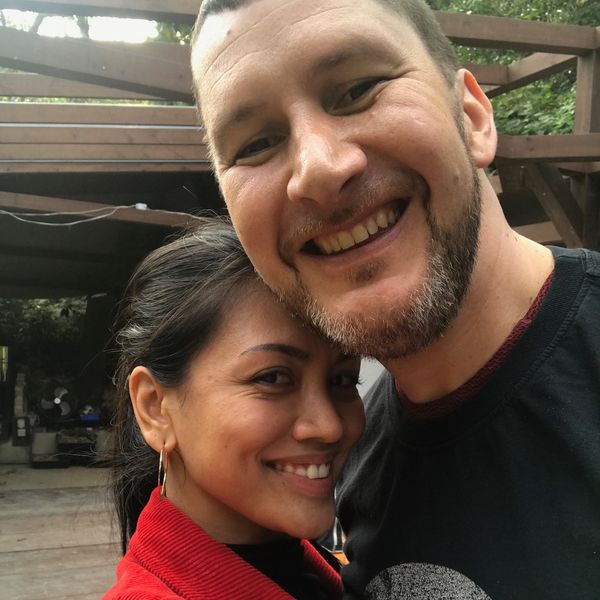 A happy couple smiling together outdoors under a wooden structure.