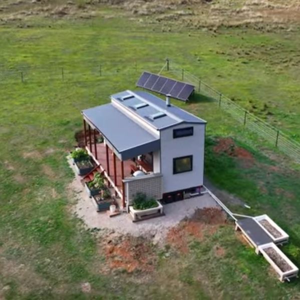 A modern tiny house with solar panels in a green field.