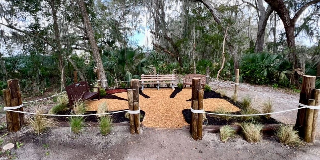Peaceful outdoor seating area in a wooded setting with benches and mulch pathways.