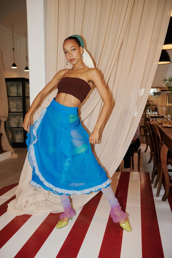 Model posing in a vibrant blue skirt with layered purple leggings and yellow heels.